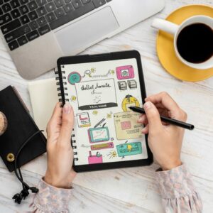 Bullet journal ao lado de um dispositivo mostrando um app de gerenciamento de projetos.